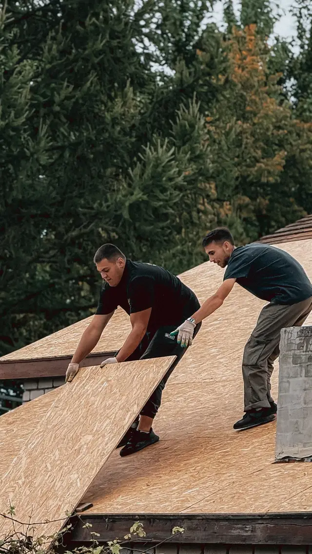 Two roofers laying plywood decking on a roof