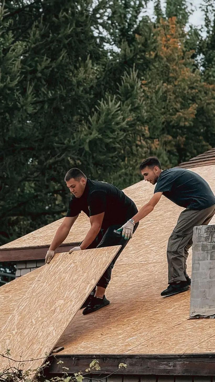 Two roofers laying plywood decking on a roof