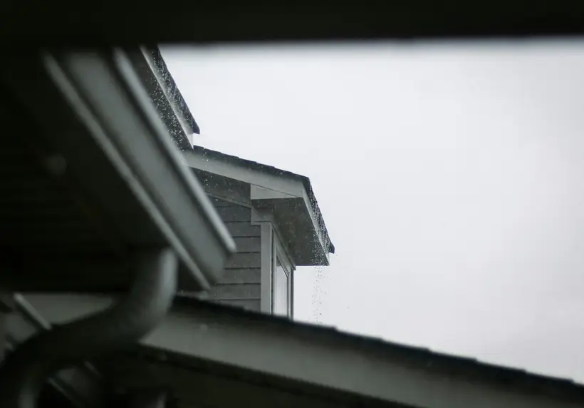 Roof edge with a gutter and downspout under a grey sky